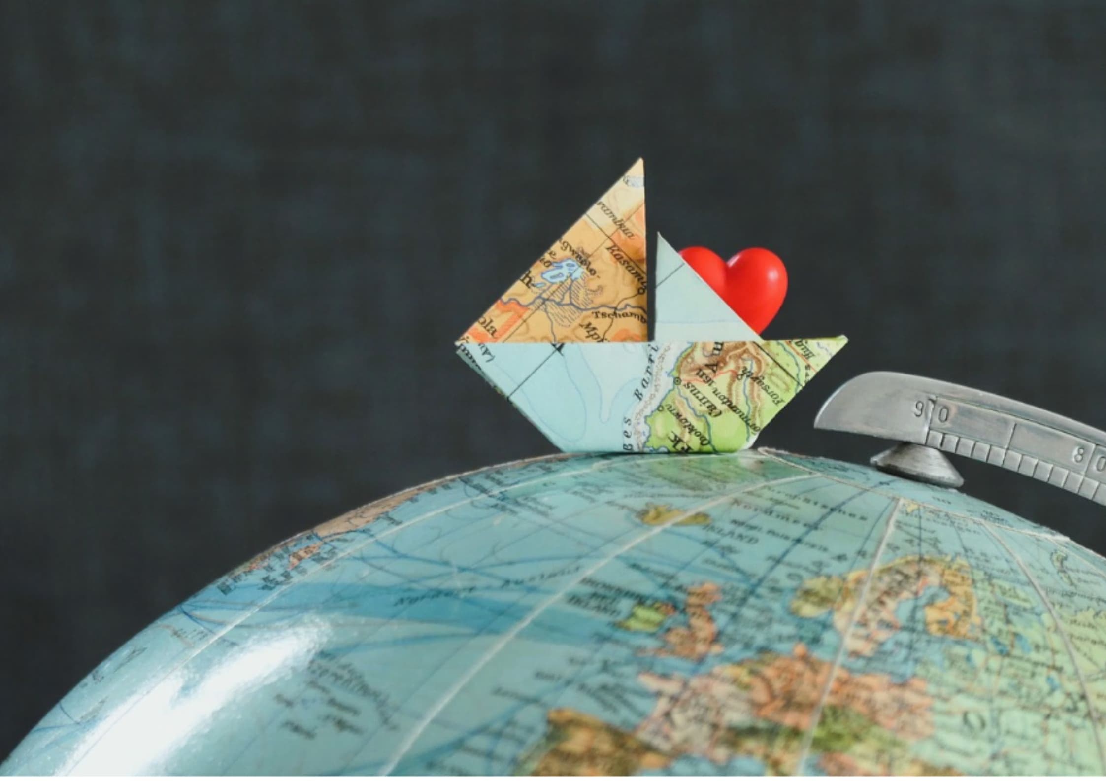 Origami boat made from a map with a red heart inside, sits atop a globe.